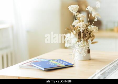 .getrocknete Blumen in einer Vase auf dem Esstisch neben Büchern. Stockfoto