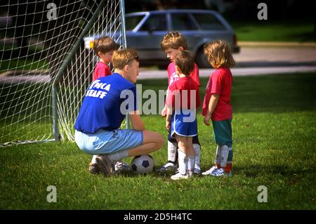 Coach unterrichtet junge Jungen und Mädchen das Spiel des Fußballs Und das Konzept der Teamarbeit Stockfoto