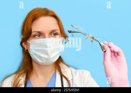 Ärztin hält Brille auf blauem Hintergrund, Nahaufnahme. Stockfoto