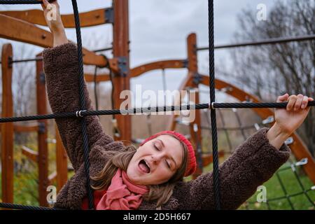 Lustige junge Frau auf einer Seilleiter. Frau, die im Herbst auf dem Spielplatz herumtollt Stockfoto