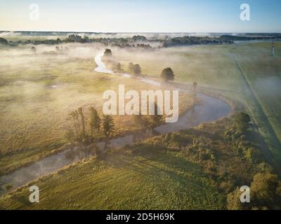 Herbst nebligen Sonnenaufgang Luftbild. Bunte neblige Morgendämmerung. Herbst ländliche Szene. Kleiner Fluss mit den Bäumen in der Wiese und dem Feld, Weißrussland Stockfoto