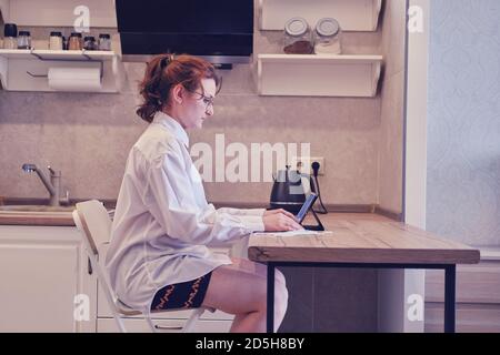 Frau arbeitet online in der Küche mit einem Tablet während Isolation durch Grippe Stockfoto