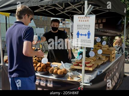 Besucher des Broadway Market, mit Straßenschildern, die darauf hinweisen, dass sie aufgrund der Coronavirus-/Covid-19-Pandemie in London, England, Großbritannien, einen sicheren sozialen Abstand halten sollten Stockfoto