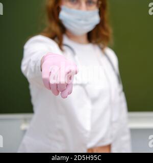 Der Schularzt in einer medizinischen Maske steht an der Tafel und zeigt auf Sie. Lernschwierigkeiten bei der Grippepandemie Stockfoto