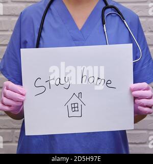 Ärztin hält ein Plakat und ruft, zu Hause zu bleiben. Krankenschwester in Schutzhandschuhen mit einem Laken in den Händen „nach Hause“ Stockfoto