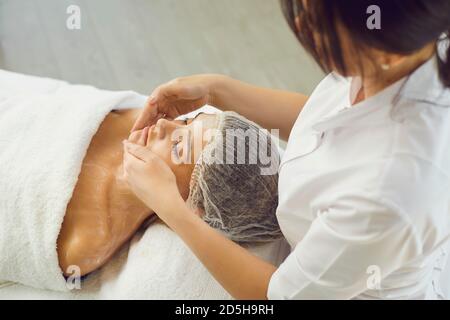 Kosmetologe Anwendung feuchtigkeitsspendende Creme Ro Womans Gesicht und Schultern während Hautpflege Stockfoto