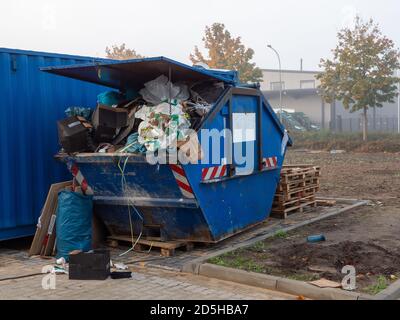 Ein blauer Abfallbehälter, gefüllt mit Baustellenabfällen, steht Auf einer Baustelle Stockfoto