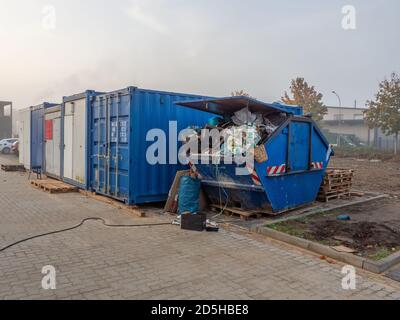 Ein blauer Abfallbehälter, gefüllt mit Baustellenabfällen, steht Auf einer Baustelle Stockfoto