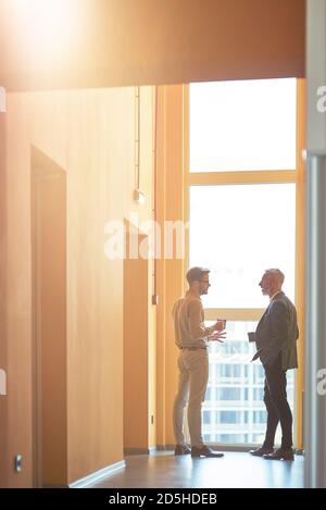 Volle Länge von zwei männlichen Kollegen stehen in der Moderne Büro und diskutieren etwas während der Kaffeepause Stockfoto