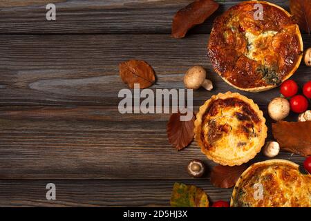 Hausgemachtes Gebäck Quiche lorraine mit Spinat, Pilzen, Tomaten und Käse auf Holztisch mit Herbstblättern. Draufsicht mit Kopierraum Stockfoto