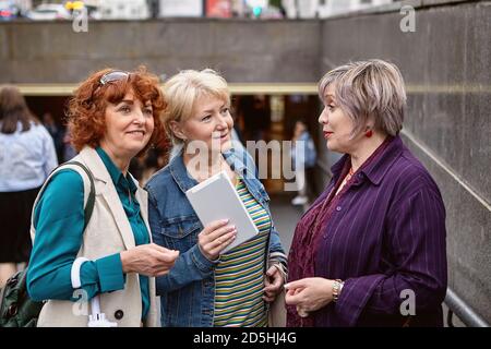 Drei ältere europäische Frauen sprechen auf der Straße in der Nähe des Abstiegs zur Unterführung. Stockfoto