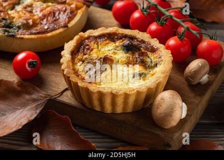 Huhn, Pilz und Tomaten Pie Quiche mit Herbstblättern auf rustikalem Holzhintergrund. Nahaufnahme Stockfoto