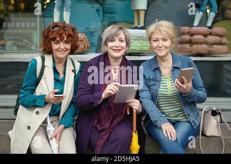 Drei weiße ältere Frauen mit mobilen Geräten in den Händen lächeln. Stockfoto