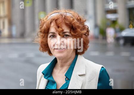 Porträt einer lächelnden europäischen älteren Frau auf der Straße einer Großstadt bei Regenwetter. Stockfoto