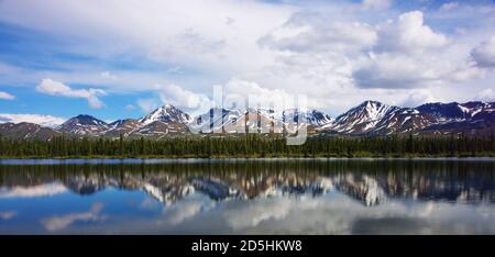 Zerklüftete schneebedeckte Berggipfel mit Schnee auf der Spitze, der sich im Frühsommer im flachen Fluss widerspiegelt. Stockfoto