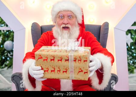 Echt authentisch überrascht Weihnachtsmann Weihnachtsmann hält Weihnachtsgeschenk. Erfüllung von Wünschen. Stockfoto