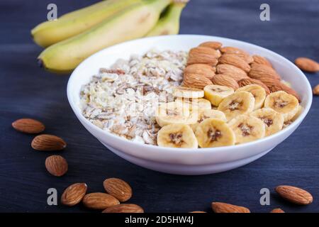 Ein Teller mit Müsli, Mandeln, Banane, Persimmon auf schwarzem Holzgrund. Nahaufnahme. Platz kopieren Stockfoto