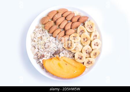 Ein Teller mit Müsli, Mandeln, Banane, Kaki isoliert auf weißem Hintergrund. Draufsicht. Stockfoto