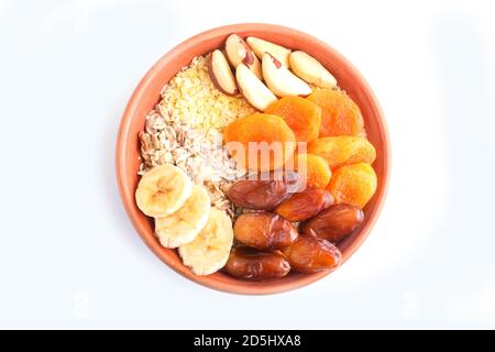 Ein Teller mit Müsli, Banane, getrockneten Aprikosen, Datteln, Paranüssen isoliert auf weißem Hintergrund. Draufsicht. Stockfoto