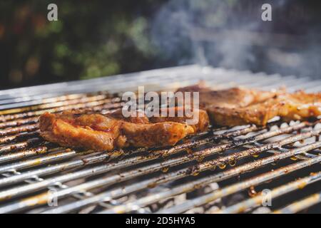 Schweinesteaks kochen über dem Grill. Seitenansicht. Rauch im Hintergrund. Stockfoto