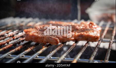 Schweinesteaks kochen über dem Grill. Seitenansicht. Rauch im Hintergrund. Stockfoto