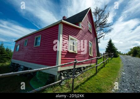 Eckansicht eines Vintage Cottage unter blauem Himmel und Wolken. Das kleine rote Holzgebäude hat mehrere doppelt aufgehängte Fenster mit einem schwarzen Dach. Stockfoto