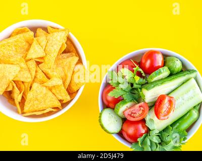 Gesunde und ungesunde Lebensmittel, Diät-Konzept. Gebratene Chips oder Nachos und grüner Sommersalat in Schüsseln isoliert auf gelbem Studiohintergrund mit Cop Stockfoto