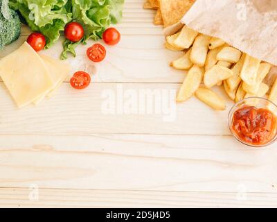 Gesunde vs ungesunde Lebensmittel, Diät-Konzept. Salat-Salat, Kirschtomaten auf der linken Seite und französisch gebratene Kartoffeln auf der rechten Seite auf Holztisch Studio b Stockfoto