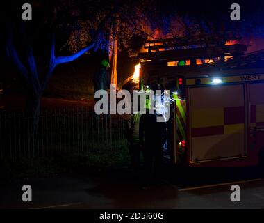 Feuerwehrleute, die nachts einen Brand in Großbritannien bekämpfen.Sie löschen ein Auto in Brand mit Hilfe von Spezialausrüstung. Stockfoto