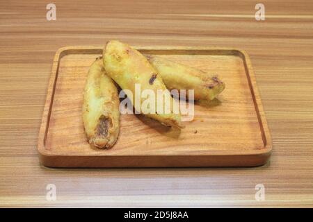 Pisang Goreng. Drei gebratene Bananen auf einem Holztablett in der Draufsicht. Stockfoto