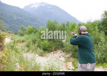 Ein Mann hält eine Schrotflinte im Abspann bereit, um auf eine Tontaube zu schießen, um sein Ziel in Squamish, British-Columbia, zu üben Stockfoto