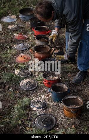 Waddewitz, Deutschland. Oktober 2019. Mathias Stein sammelt aus den Töpfen Raku-Schüsseln, in denen die Schüsseln nach dem Brennen mit reduziertem Sauerstoff abkühlen. Einmal im Jahr feuert Keramiker Mathias Stein Teeschalen mit einer gesprungenen Glasur - ein Craquelé - in einem hausgemachten Holzofen an. Die feinen Risse werden durch den Temperaturabfall verursacht, wenn die glühenden Schüsseln mit langen Zangen aus dem Ofen gezogen werden. Die spezielle Brenntechnik stammt aus Japan und wird Raku genannt. Quelle: Sina Schuldt/dpa/Alamy Live News Stockfoto