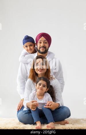 SIKH FAMILIE SITZT AUF DEM TEPPICH ZUSAMMEN IN GLÜCK UND BEQUEM POSIEREN Stockfoto