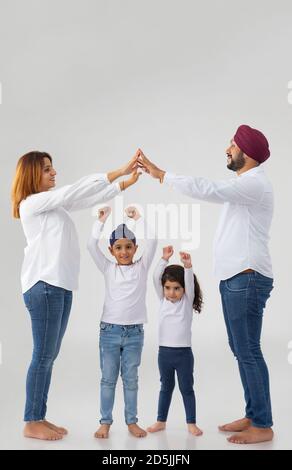 SIKH MANN UND FRAU, DIE HAUS, INDEM SIE HÄNDE MIT SOHN UND TOCHTER SPIELEN DARUNTER Stockfoto