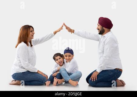 SIKH BRUDER UND SCHWESTER UMARMTEN EINANDER LACHEN, WÄHREND MUTTER VATER SITZT UND HÄLT DIE HÄNDE, UM HAUS ZU MACHEN Stockfoto