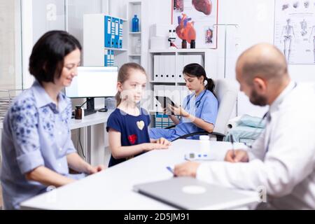 Krankenschwester mit Tablet-pc, während der Arzt das kranke Kind im Krankenhaus konsultiert. Stockfoto