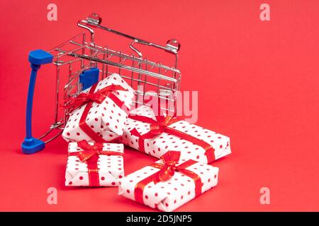 Ein umgedrehter Einkaufskorb voller Geschenke auf einem roten Hintergrund mit Kopierplatz. Konzept für weihnachten, Feiertage, Rabatte und Shopping. Stockfoto