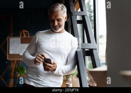 Casual Grey-haired Reifen Geschäftsmann mit Smartphone stehen am Fenster. Stockfoto