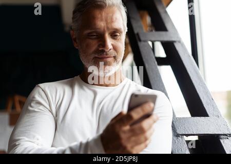 Casual Grey-haired Reifen Geschäftsmann mit Smartphone stehen am Fenster. Stockfoto