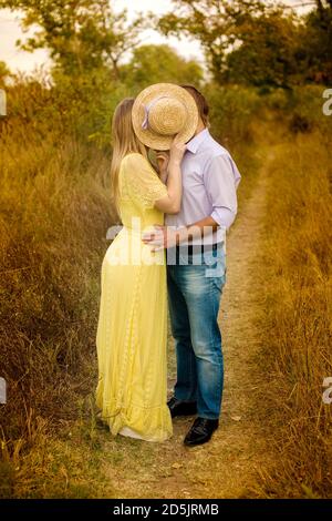 Bild von einem Kerl und ein Mädchen küssen in der park versteckt sich hinter einem Strohhut Stockfoto