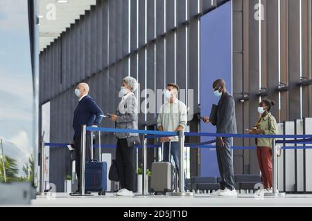 Gruppe von Menschen in Schutzmasken in einer Schlange stehen Am Flughafen Stockfoto