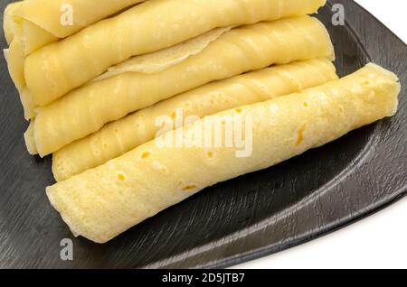 Nahaufnahme eines Stapels gerollter Maida Dosa gefüllt mit Gesüßte geriebene Kokosnuss auf einem schwarzen Teller Stockfoto