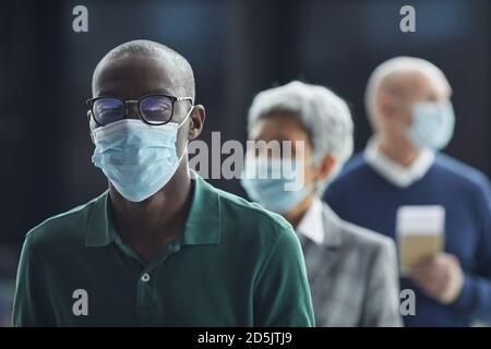 Porträt eines jungen Afrikaners in Brillen und in Schutzkleidung Maske mit Blick auf die Kamera in der Warteschlange Stockfoto
