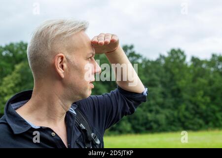 Der grauhaarige Mann, der seine Augen mit der Hand vor der Sonne schließt, sieht Stockfoto