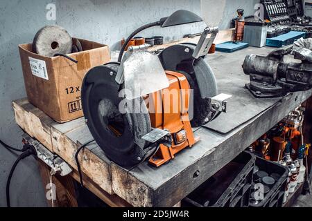 Sander-Maschine auf einer großen Werkbank, mit einem Schraubstock und einem professionellen Satz von Werkzeugen. Schleifmaschine Nahaufnahme in einer Autowerkstatt. Garage für Motorrad r Stockfoto