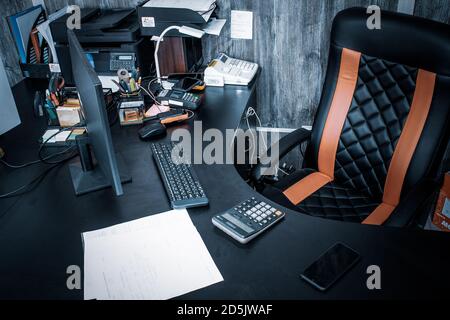 Arbeitsplatz am Tisch im Büro mit Computer, Rechner, Telefon, Kasse. Maus, Tastatur, Monitor und großer Lederstuhl. Persönlicher Bereich in Stockfoto