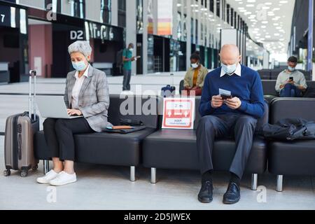 Gruppe von Menschen in Masken sitzen im Warteraum sie Soziale Distanz bewahren Stockfoto