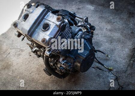 Alter Motorradrotor in einer Werkstatt isoliert, Nahaufnahme. Motorrad gebrochener Metallmotor liegt auf einem Zementhintergrund in der Garage. Reparatur, Wiederherstellung. Stockfoto
