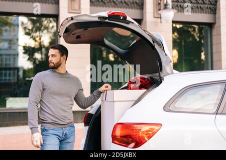 Porträt eines bärtigen jungen Lieferers in legerer Kleidung, der in der Nähe des Autos steht. Stockfoto