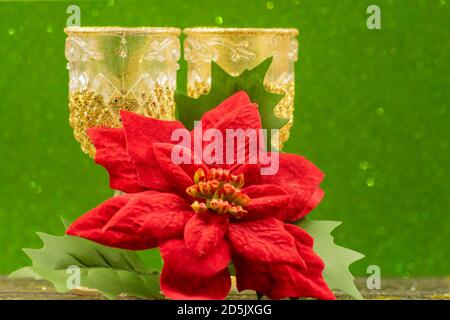 Zwei Gläser Champagner und rote Blume auf Weihnachtsstern auf grünem, glitzerndem Hintergrund. Festliche Grußkarte für das neue Jahr Stockfoto